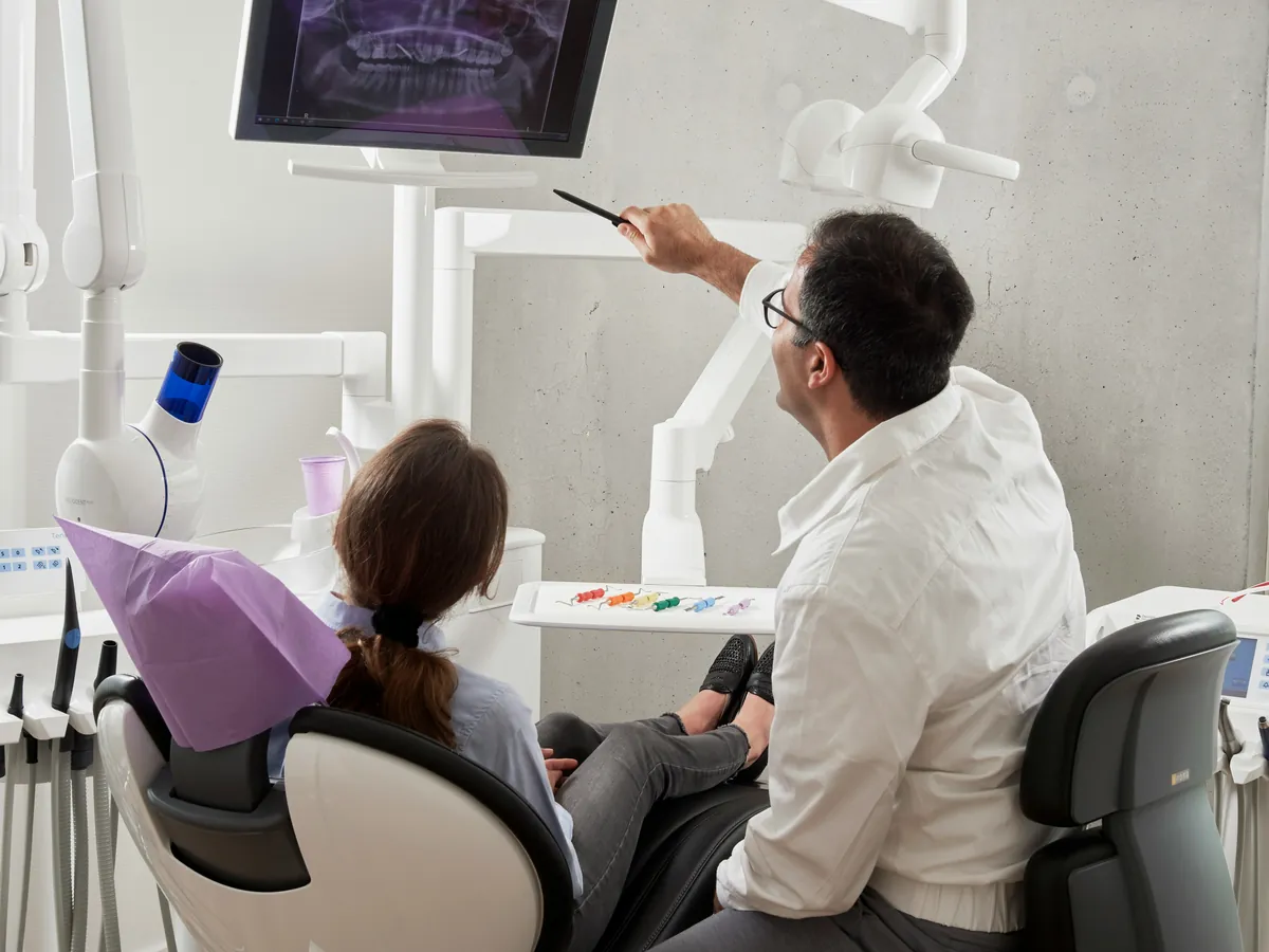 Dentist pointing to an X-ray on a screen while explaining it to a patient in the dental chair